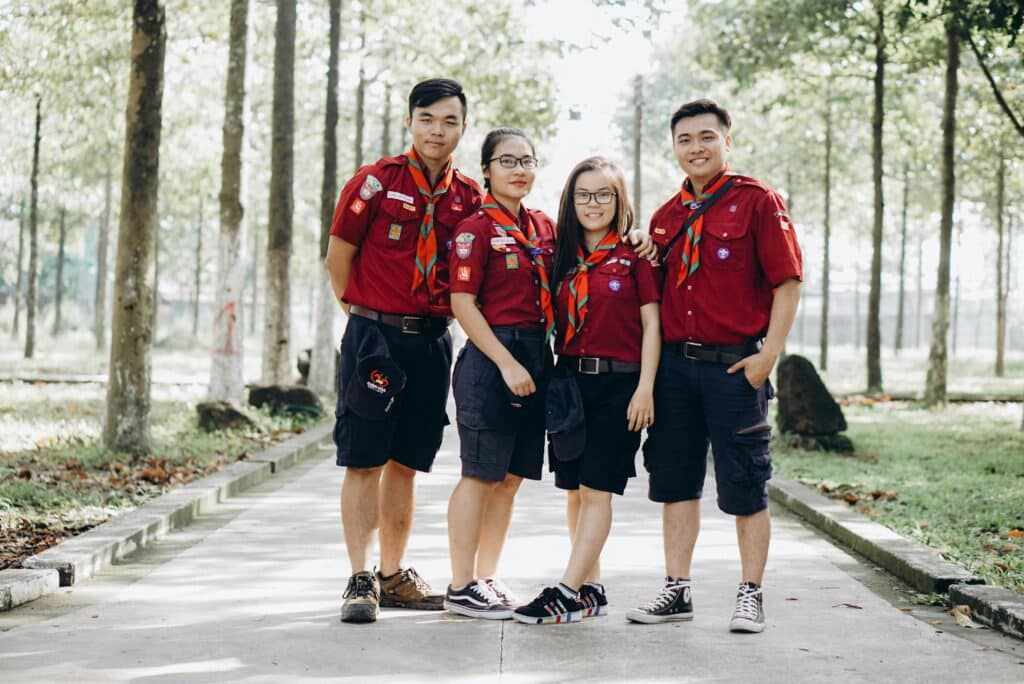 Four scouts in uniform stand together in a forest setting, smiling.