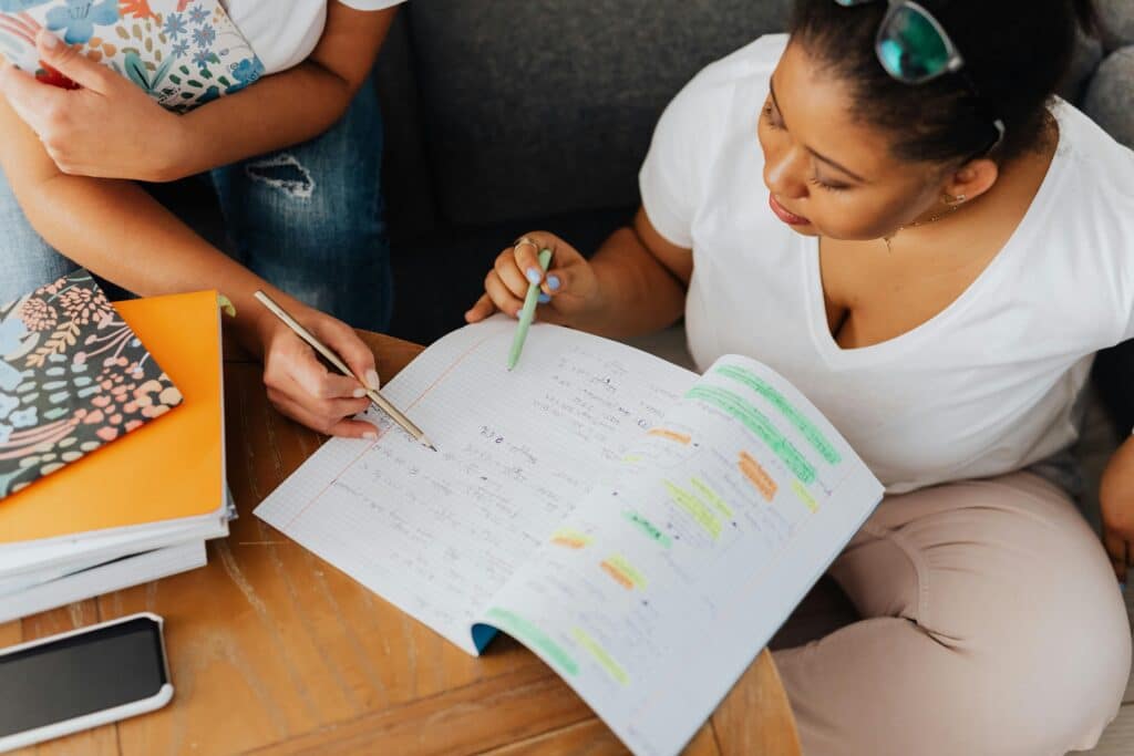 Two adults collaborate on educational content with notebooks and pens indoors.