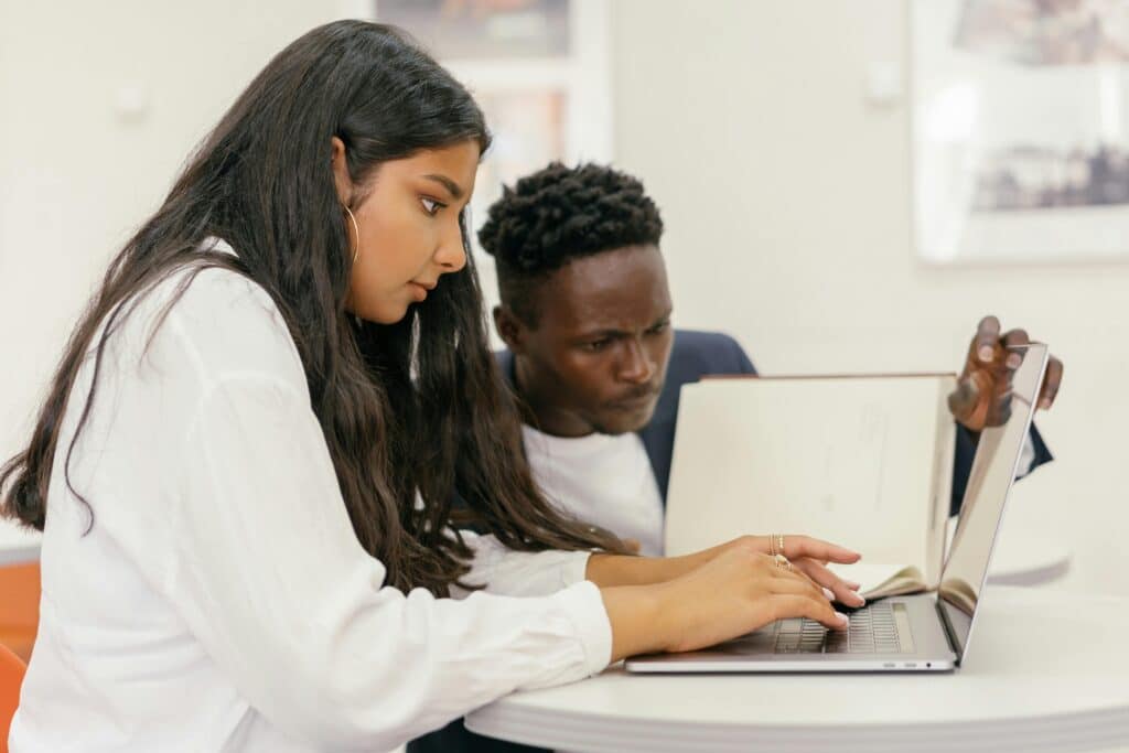 Two students collaborating on a laptop in a study setting, absorbed in research.