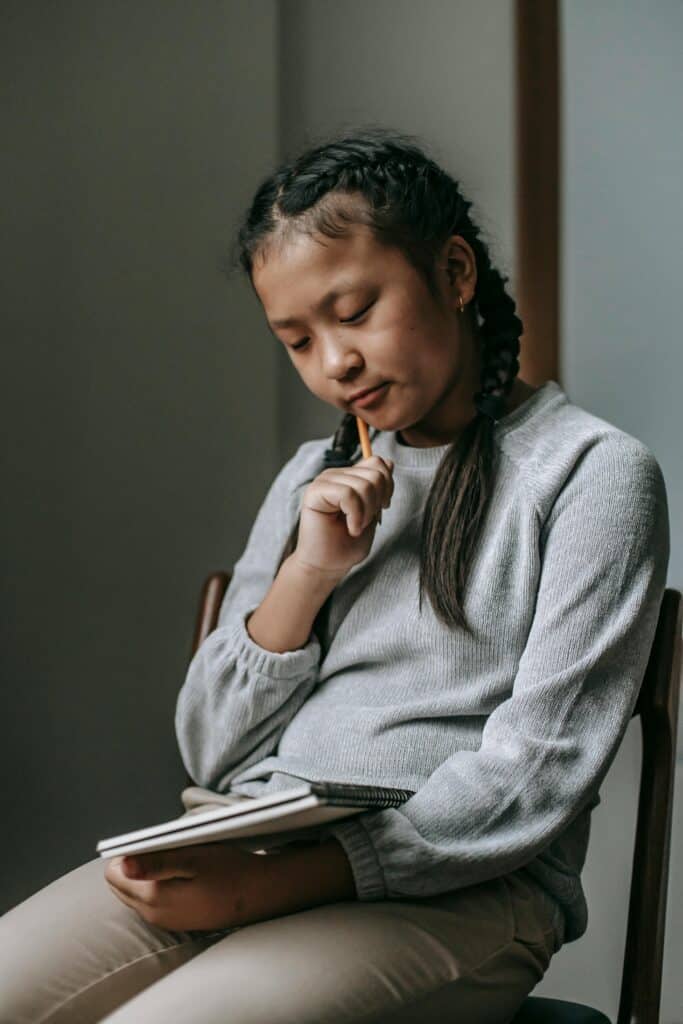 Pensive teenager writing thoughts in a notebook at school, showcasing deep focus.