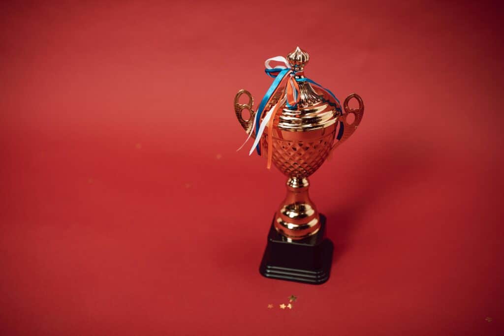 Golden trophy cup with red, blue, and white ribbons on a red backdrop symbolizes achievement and success.