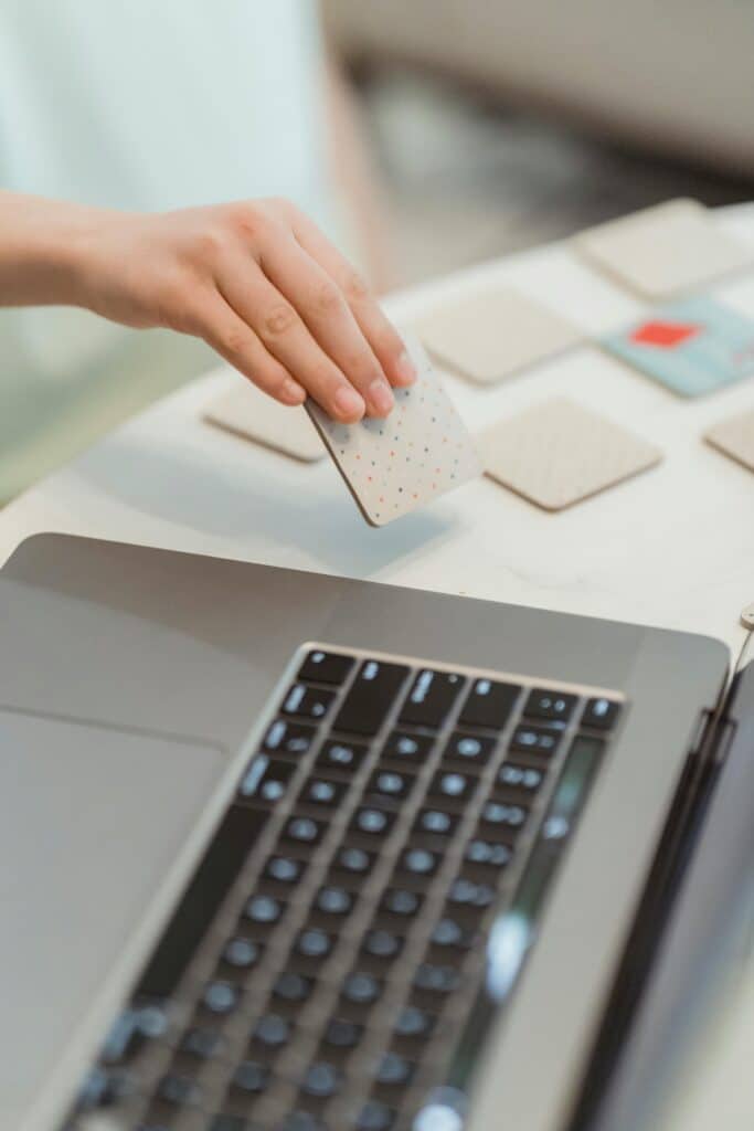Close-up of a hand holding a playing card next to a laptop, illustrating technology interaction.