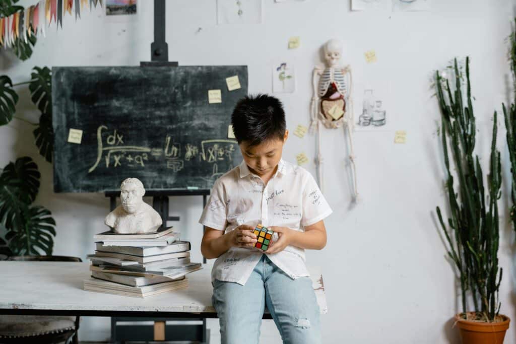 Asian boy solving Rubik's Cube in a classroom, with books and educational materials around.
